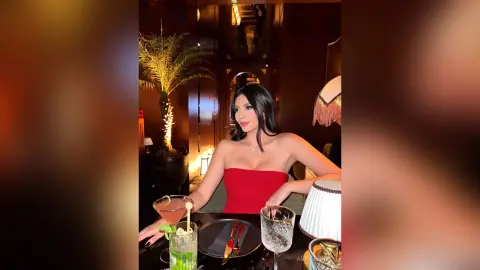 Elegant woman in a red strapless dress enjoying a cocktail at a moody, dimly lit upscale lounge.