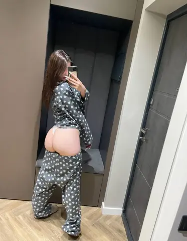 Young woman in grey heart-patterned pajamas taking a mirror selfie in a modern minimalist room.