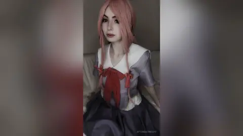 Cosplayer with pink hair wearing a Sailor Moon inspired outfit sitting in a soft, dreamy indoor setting.