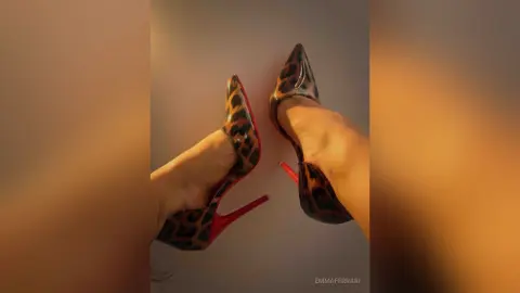 Close-up of leopard print high heel pumps with red soles worn by a person in warm lighting.