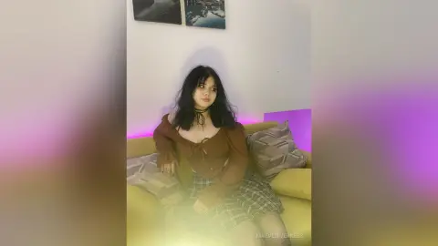 Young woman in a brown top and plaid skirt sitting on a sofa with moody purple ambient lighting.