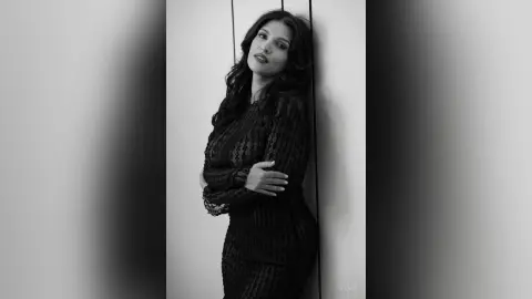 Elegant woman in a black lace dress posing against a minimalist wall in a moody black and white portrait.