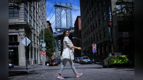 Stylish woman in a white jacket and patterned pants walking on a New York City street near the Manhattan Bridge.