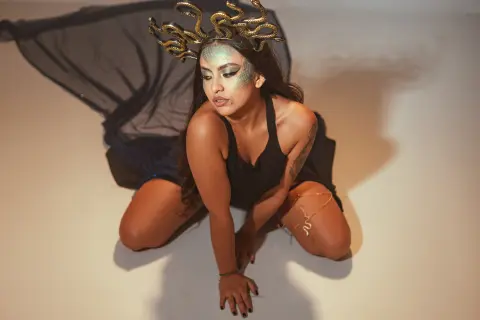 Woman in black outfit and gold snake headpiece posing with mystical goddess makeup in a studio setting.