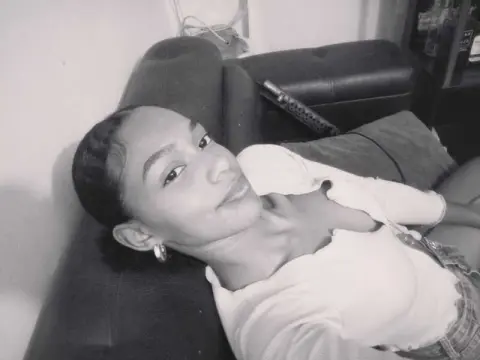 Young woman in a white top relaxing on a dark sofa in a moody black and white indoor setting.