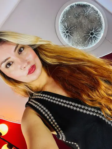 Ninablaze27 with long blonde and red hair wearing a black studded top, looking at the camera.
