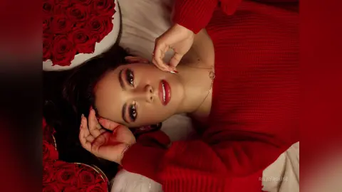 Beautiful woman in a red sweater lying next to red roses for a romantic and moody aesthetic portrait.