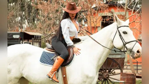 FlorenciaCopper sits astride a white horse wearing a white button-down shirt and black leggings.