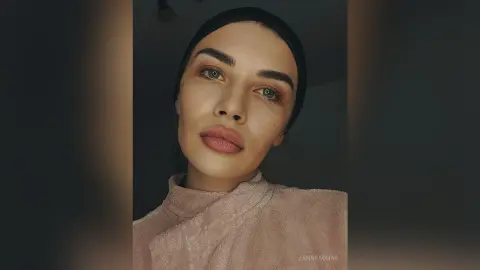 JanneMaine poses for a close-up selfie wearing a black headwrap and a light pink textured towel or wrap around her neck.