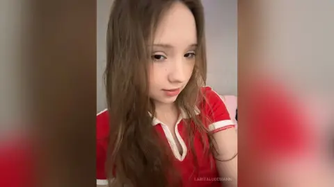 LaritaLudemann looks at the camera wearing a red short-sleeved shirt with a white collar.