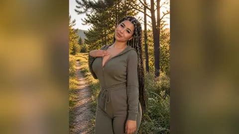 Smiling woman in olive green jumpsuit standing on a forest path during a golden hour sunset.