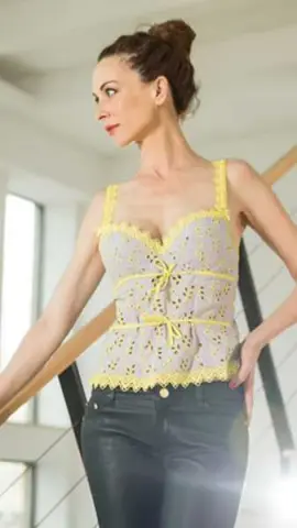 Elegant woman in a yellow lace camisole and dark jeans posing in a bright, modern interior.