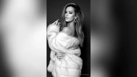 Elegant woman in a luxurious white faux fur coat posing for a glamorous black and white studio portrait.