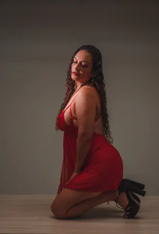Curvy woman in a red slip dress posing elegantly against a neutral studio background.