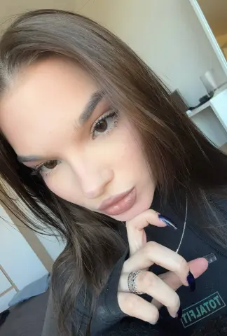 Noirbeauty poses with her hand under her chin, showing her long brown hair, dark eyes, and long blue nails.