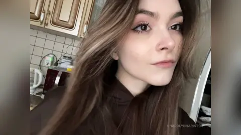 Young woman with long brown hair wearing a dark turtleneck in a bright kitchen setting.