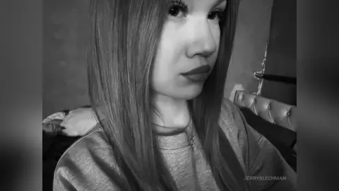 Portrait of a young woman with long straight hair wearing a casual sweatshirt in a moody black and white setting.