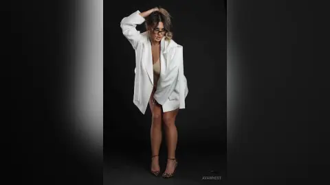 Stylish woman in a white oversized blazer and beige bodysuit posing against a dark studio background.