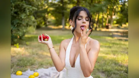 Young woman in a white halter dress eating fresh strawberries on a sunny summer picnic blanket.