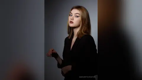 Elegant woman in a black blazer posing with a sophisticated mood against a neutral studio background.