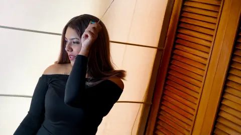 Young woman in a black off-the-shoulder top posing thoughtfully against a warm wooden shutter background.