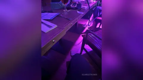 A person sitting at a wooden desk with papers under moody purple ambient lighting in a dim room.