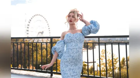 DaisyLin poses outdoors in a light blue off-the-shoulder lace dress with her blonde hair styled in a bun.