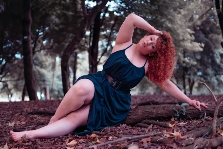 IsadiaRousso poses with her red curly hair spread out, showing her face and bare shoulders against a dark background.
