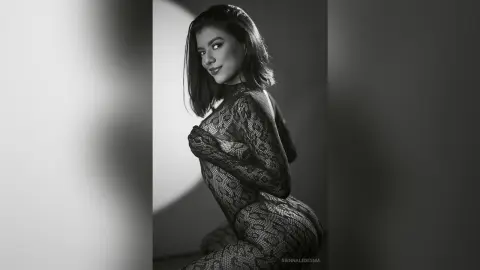 Elegant woman in a black lace bodysuit posing in a moody, cinematic black and white studio portrait.