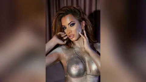 FelishaRose poses with her hands near her face, wearing a silver glittery micro-bikini top that covers her nipples.