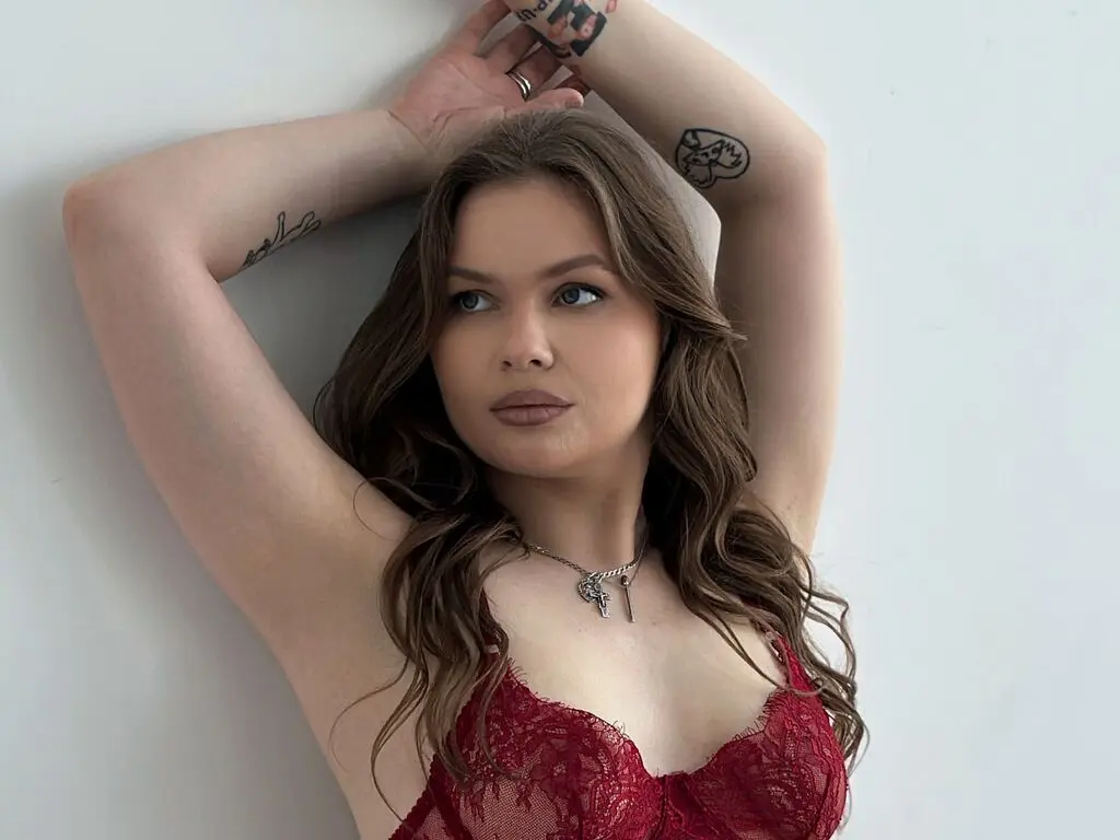 Brunette woman in red lace lingerie posing against a white wall with a relaxed, moody aesthetic.