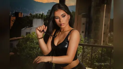 Glamorous woman in a black leather top posing on a city balcony during golden hour sunset.