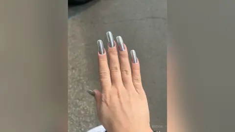 Close-up of a hand featuring long metallic silver chrome stiletto nails against a neutral concrete background.
