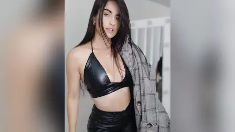 Young woman in a black leather halter top and matching trousers posing in a stylish, modern indoor setting.