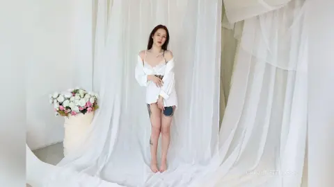 Young woman in white lace lingerie and an open shirt posing in a dreamy, bright white studio setting.