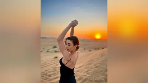 Dreamy portrait of a woman in a black tank top posing against a golden desert sunset sky.