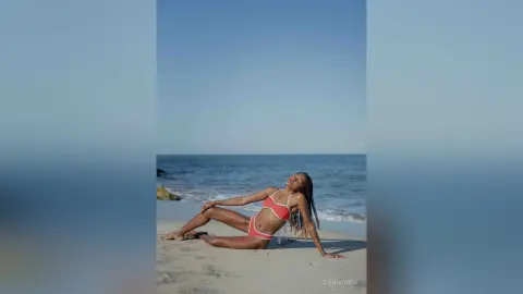 Young woman in a red bikini relaxing on a sunny beach with ocean waves in the background.