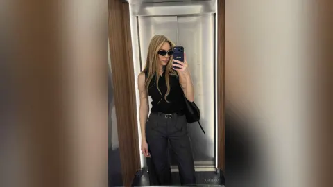 AmiliRay — AmiliRay takes a mirror selfie in an elevator wearing a black sleeveless top, dark trousers, and sunglasses.