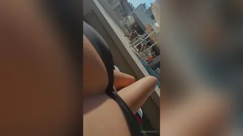 Close-up of a woman in black swimwear relaxing outdoors on a sunny day near urban buildings.