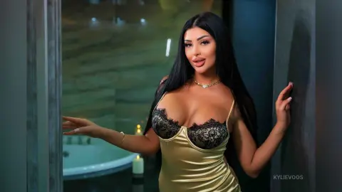 Glamorous woman in a gold satin dress posing in a luxury bathroom with moody lighting.