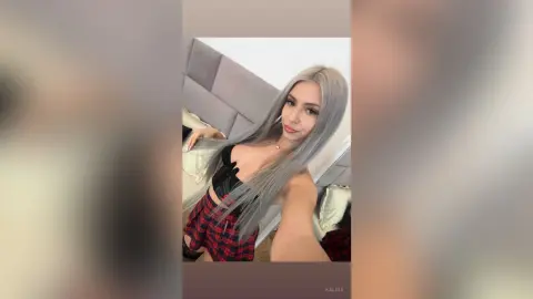 Kalira poses in a red plaid skirt and black top, showing off her long silver hair and slim figure.