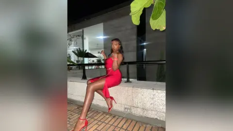 Elegant woman in a red evening dress sitting on a balcony at night for a glamorous summer look.