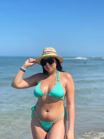 Curvy woman in a turquoise bikini and straw hat posing on a sunny beach by the ocean.