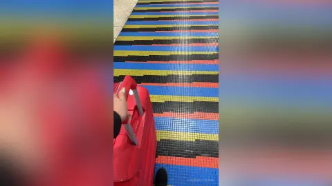 Close-up of a red suitcase being pulled across a colorful striped mosaic tile floor.