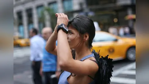 Stylish woman in a blue top and black feathered wings walking on a busy city street near a yellow taxi.