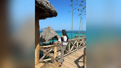 Woman in white blouse and patterned trousers relaxing on a tropical wooden pier overlooking turquoise ocean waters.