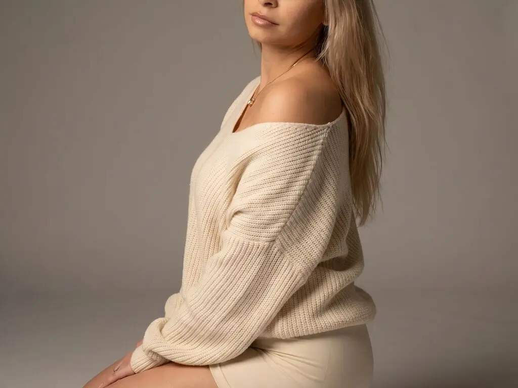 Blonde woman in a cozy cream knit sweater sitting against a neutral studio background with a soft mood.