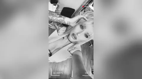 Blonde woman in a white shirt posing for a selfie in a moody, cinematic black and white film aesthetic.