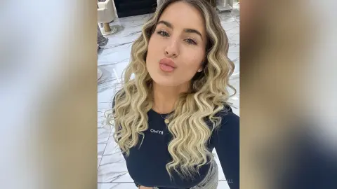 Smiling blonde woman in a navy blue graphic t-shirt posing in a bright marble-floored salon.