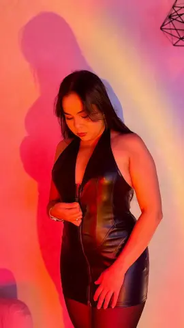 Woman in a sleek black leather halter dress posing under warm red and yellow studio lighting.